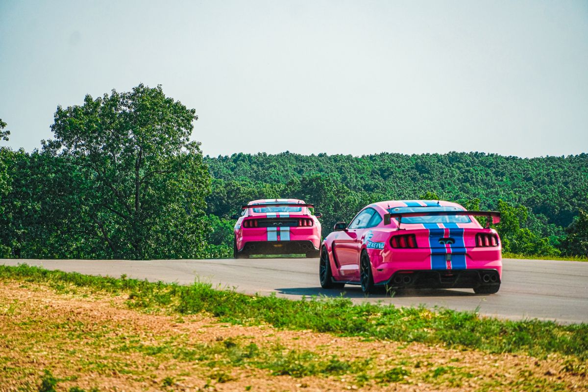 Two pink racecars rounding a corner at the OIR track